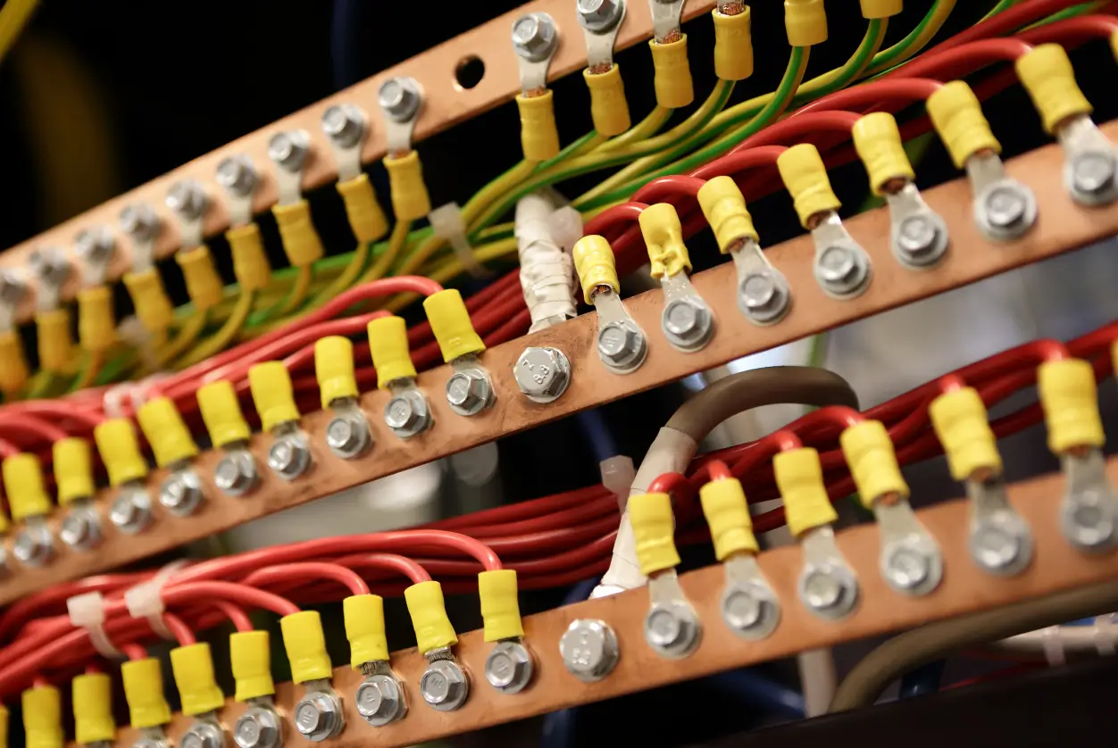 Close-up of electrical terminal blocks with copper bars and multiple connected wires using yellow insulated connectors.
