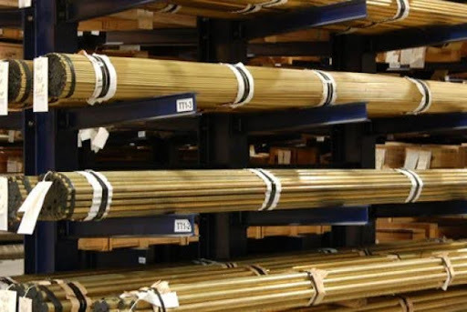 Bundled brass round bars stored on cantilever racks in a metal warehouse.