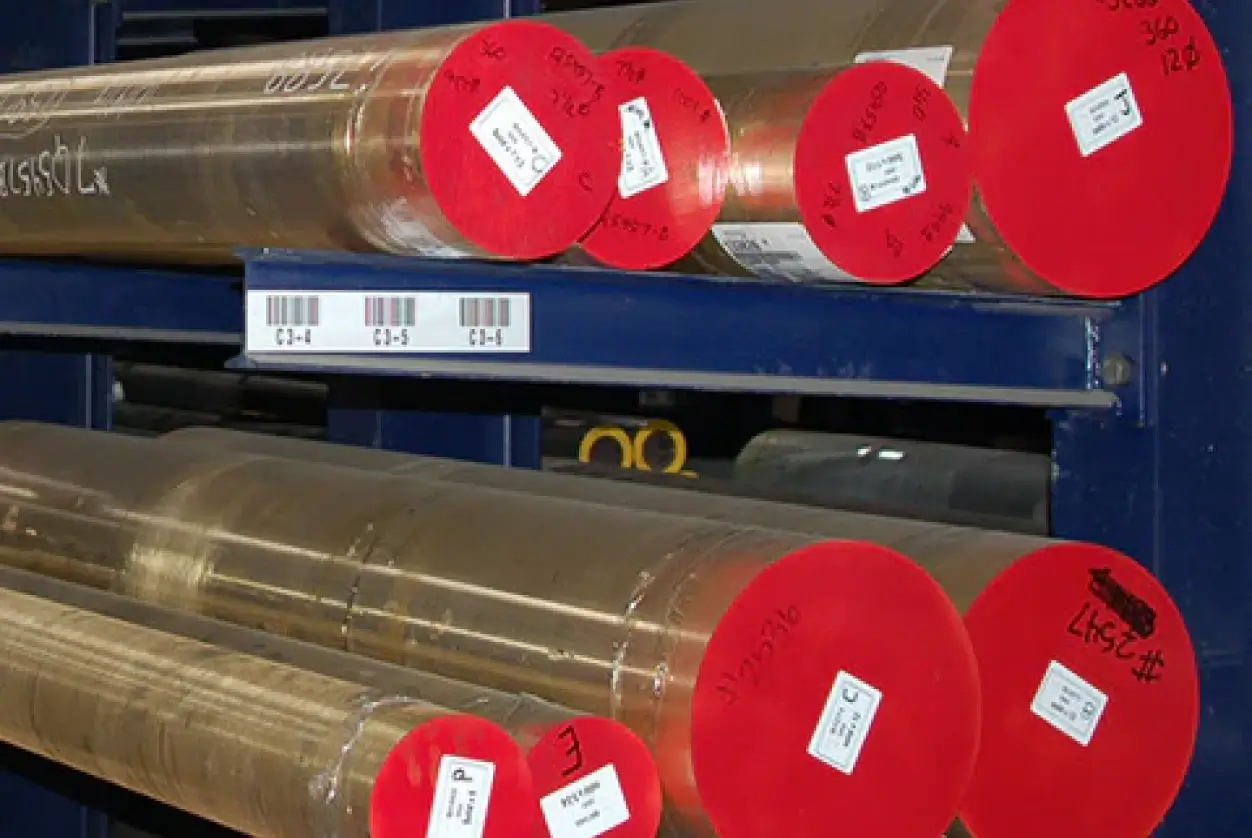 Brass round bars with red-painted ends and identification labels stored on industrial metal shelving.